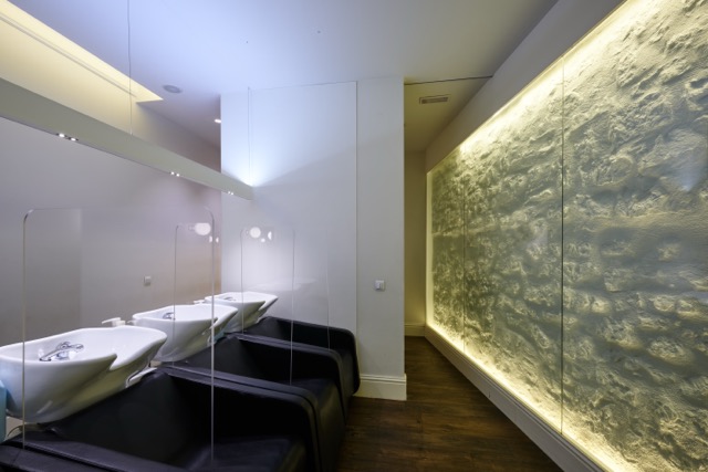 Rubén Hernáez Peluqueros - Peluquería En Vara De Rey, Logroño Zona De Lavado De Cabello Con Tres Lavacabezas Y Pared De Piedra Retroiluminada En Rubén Hernáez Peluqueros